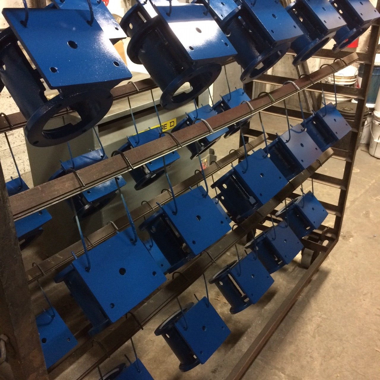 Blue painted parts racked on a paint line at Quality Metal Finishing